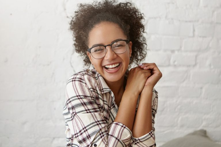 woman with glasses smiling against white brick background